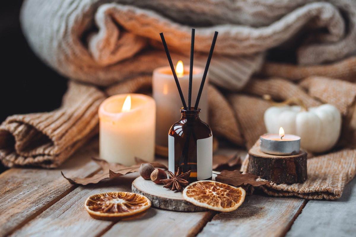 A lit candle with a pumpkin, knitwear, dry leaves, cinnamon and star anise in warm light