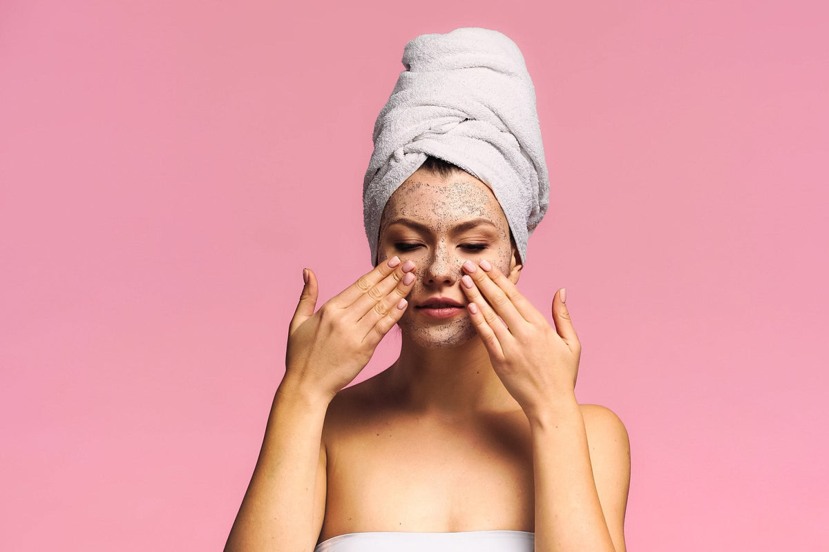 A young woman with a towel on her head applying an exfoliating mask
