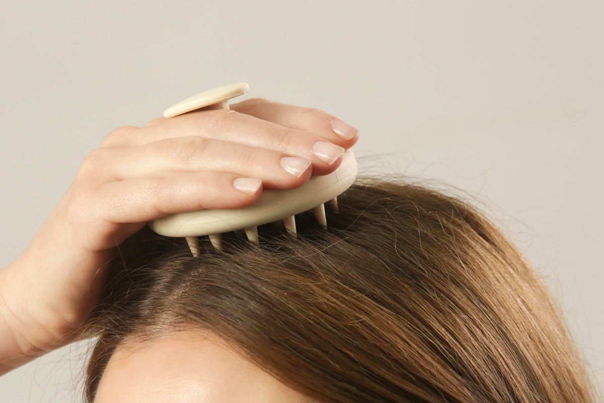 A woman massaging her scalp with a scalp massager