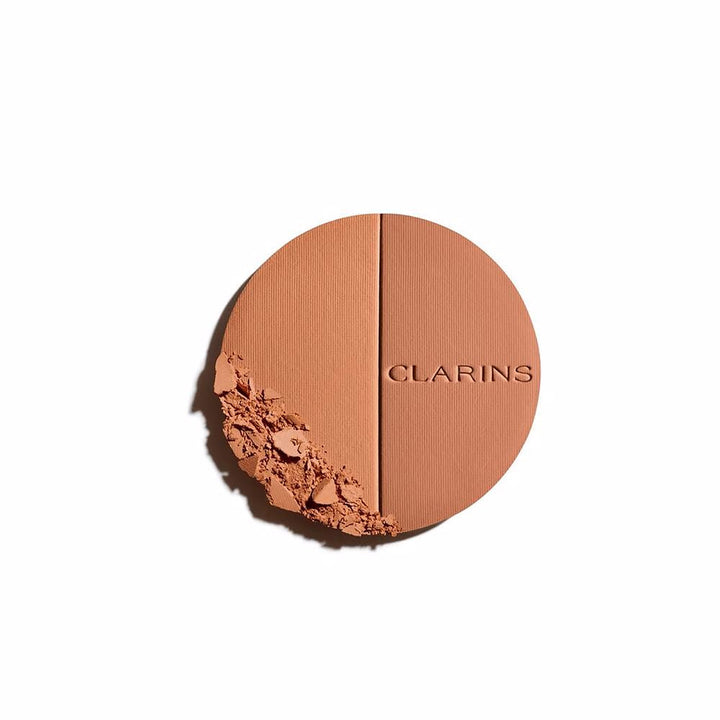 Clarins Round orange compact powder case with metallic rim, embossed brand name, minimalist metal/plastic finish